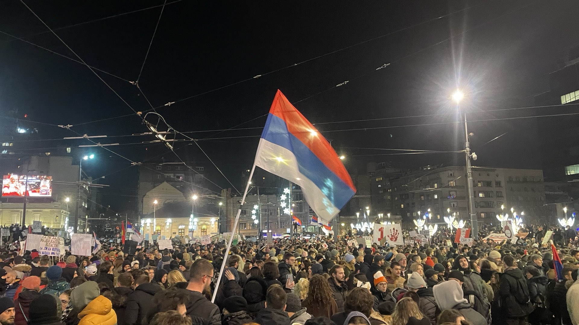 Ноћни протест на Тргу Славија у Београду 22. децембра 2024: велика српска застава изнад масе људи.
